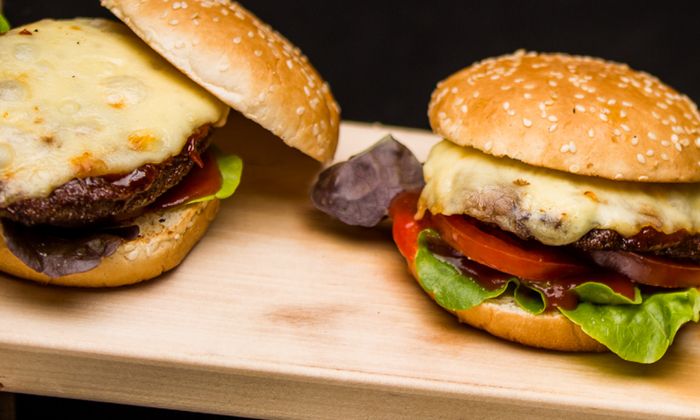 Emmentaler Rezept Klassischer Cheeseburger mit Emmentaler von GOLDSTEIG, Hackfleisch, Salat und Tomate auf Holzbrett 