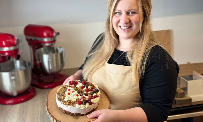 Rezepte & Inspirationen: Monika Nagl zeigt lächelnd ihre weihnachtliche Himbeer-Lebkuchen-Torte mit Mascarpone und Butter auf einer Tortenplatte aus Holz.