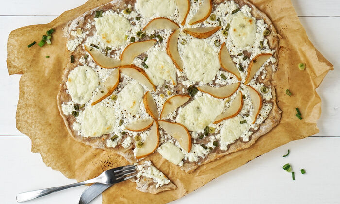 Protinella Rezept Birne-Protinella Flammkuchen mit körnigem Frischkäse und Frühlingsziebel von GOLDSTEIG auf Backpapier