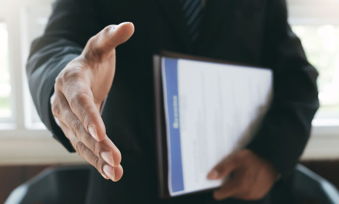 Zu Ihrer Bewerbung/initiativ: Ein Recruiter streckt seine Hand nach vorne zum Handschütteln und trägt dabei einem Anzug in schwarz