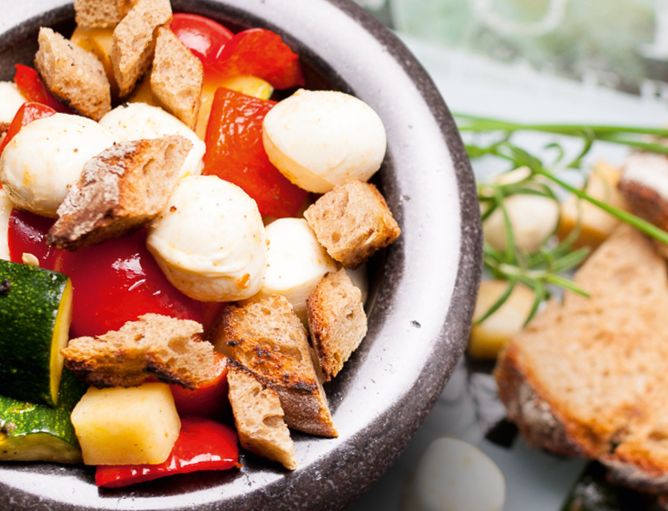 Aktionen und Neues: Salat einfach lecker - GOLDSTEIG Käsespezialitäten Salat in Steinschüssel mit Zucchini, Papika, Brot und Karotten, dazu Bambini Mozzarella Mini von GOLDSTEIG neben Brot und Kräutern