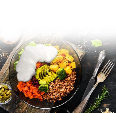 Bowl mit Mozzarella von GOLDSTEIG, Avocado, Paprika, Salat und Brokkoli in Glasschale auf Holzbrett, daneben Besteck