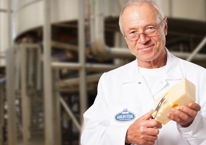Mozzarella Käsefacts vom GOLDSTEIG Käsemeister - GOLDSTEIG Käsespezialitäten Käsemeister mit einem Stück Emmentaler in der GOLDSTEIG Käserei