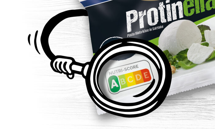 Nutri-Score / Nutri-Score Rechner / Gesundheit & Region (Gesundheit-Region) / Startseite (GOLDSTEIG) / Aktionen & Neues (Aktionen-Neues) / Ab wann ist der Nutri-Score auf allen Lebensmittel-Verpackungen in Deutschland zu finden? / Was bildet der Nutri-Score nicht ab?: Weißer Hintergrund mit Holzoptik. Darauf ist eine GOLDSTEIG Protinella 100g Verpackung mit einem illustrierter Arm zu sehen, welcher mit der Lupe den Nutri-Score A auf der Verpackung hervorhebt.