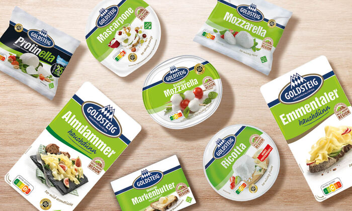 Käsesorten von GOLDSTEIG auf einem Holztisch. Protinella Kugel, Almdammer Scheiben hauchdünn, Mozzarella Bambini classic, Mascarpone, Mozzarella Kugel classic, Emmentaler Scheiben hauchdünn, Ricotta und Butter.