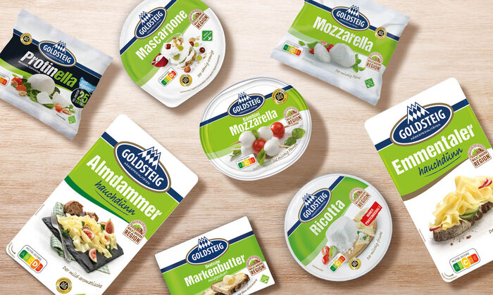 Käsesorten von GOLDSTEIG auf einem Holztisch. Protinella Kugel, Almdammer Scheiben hauchdünn, Mozzarella Bambini classic, Mascarpone, Mozzarella Kugel classic, Emmentaler Scheiben hauchdünn, Ricotta und Butter.