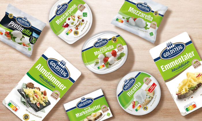 Käsesorten von GOLDSTEIG auf einem Holztisch. Protinella Kugel, Almdammer Scheiben hauchdünn, Mozzarella Bambini classic, Mascarpone, Mozzarella Kugel classic, Emmentaler Scheiben hauchdünn, Ricotta und Butter.