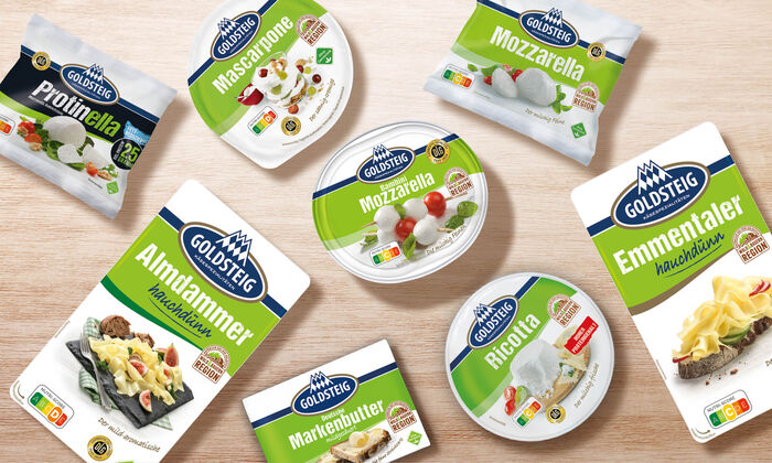 Käsesorten von GOLDSTEIG auf einem Holztisch. Protinella Kugel, Almdammer Scheiben hauchdünn, Mozzarella Bambini classic, Mascarpone, Mozzarella Kugel classic, Emmentaler Scheiben hauchdünn, Ricotta und Butter.