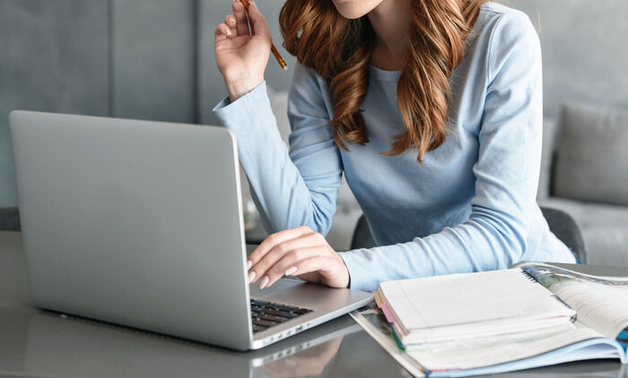 Zu Ihrer Bewerbung/eingegangen: Bewerberin sitzt am Esszimmertisch und schaut auf ihrem Laptop, daneben liegt ein Buch.