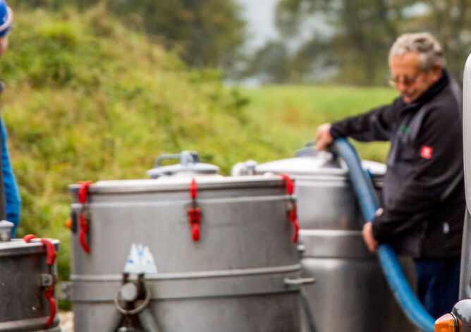 Milchsammelwagen-Fahrer saugt Milch aus mobilem Milchtank, Landwirt steht daneben