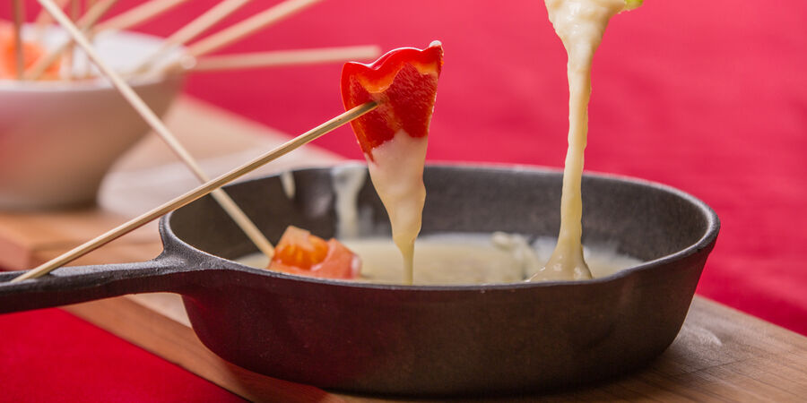 Tipp: Mit Kochen und Backen auf Nummer sicher - GOLDSTEIG Käsespezialitäten Käsefondue von GOLDSTEIG in Gusspfanne mit Gemüsestückchen auf Holzstäbchen