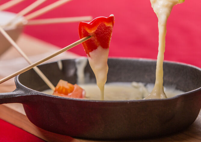 Tipp: Mit Kochen und Backen auf Nummer sicher - GOLDSTEIG Käsespezialitäten Käsefondue von GOLDSTEIG in Gusspfanne mit Gemüsestückchen auf Holzstäbchen