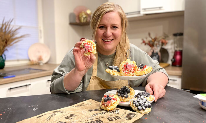 Rezepte & Inspirationen: Monika Nagl zeigt lächelnd ihre Tartelettes zum Valentinstag mit Mascarpone von GOLDSTEIG. Die Tartelettes sind mit Heidelbeeren und Zuckerherzen dekoriert.