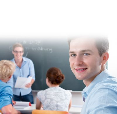 Infos zur Bewerbung: Ein Schüler blickt sitzend im Klassenzimmer über seine Schulter in die Kamera. Im Hintergrund sieht man seine Schulkameraden.