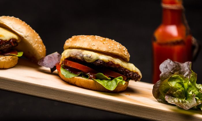 Emmentaler Rezept Klassischer Cheeseburger mit Emmentaler von GOLDSTEIG, Hackfleisch, Salat und Tomate auf Holzbrett 