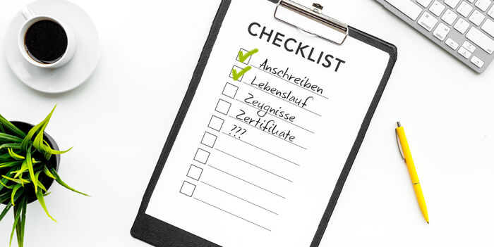 Zu Ihrer Bewerbung/Unterlagen: Checkliste liegt auf einem weißen Tisch, zusammen mit einem Stift, Computertastatur, Kaffee und einer Pflanze