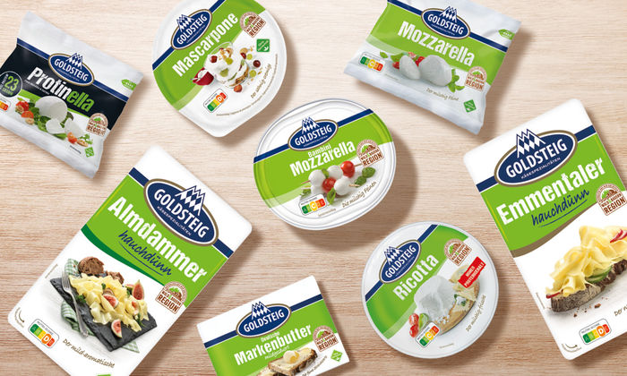 Käsespezialitäten: Käsesorten von GOLDSTEIG auf einem Holztisch. Protinella, Almdammer Scheiben hauchdünn, Mozzarella Bambini classic, Mascarpone, Mozzarella Kugel classic, Emmentaler Scheiben hauchdünn, Ricotta und Butter.
