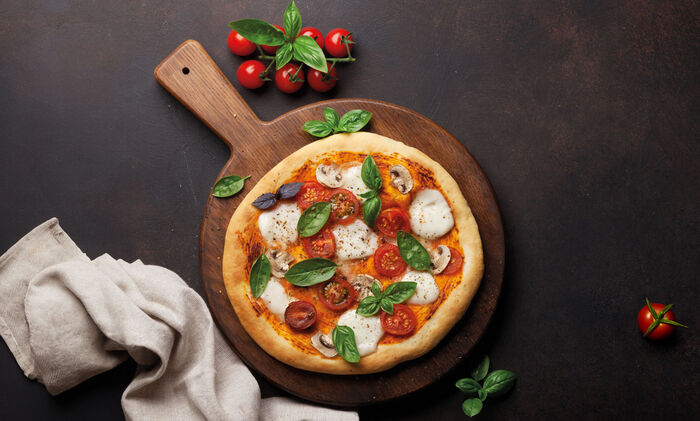 Was bedeutet eigentlich/Fior di latte: Eine Pizza mit Mozzarella fior di latte, Basilikumblätter, Tomaten und Pilzen drapiert auf einem Holzbrett.