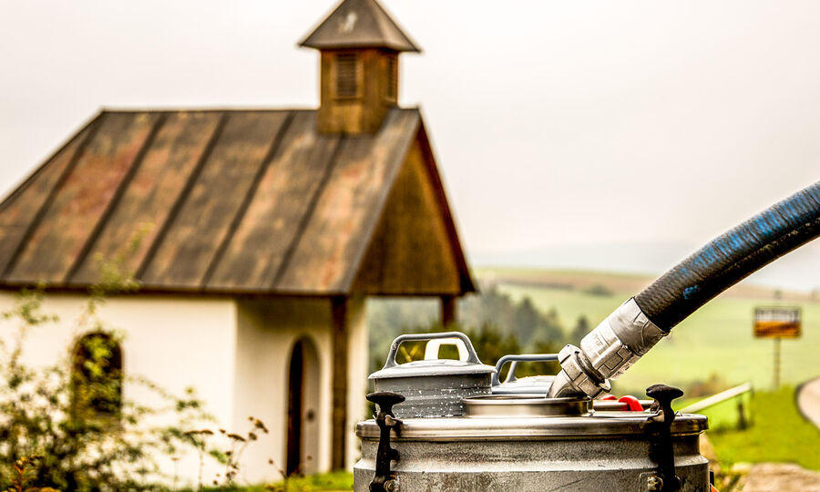 Natürlichkeit und Verantwortung: Natürlich aus Bauernhand - GOLDSTEIG Käsespezialitäten Milchabholung, im Hintergrund kleine Kapelle