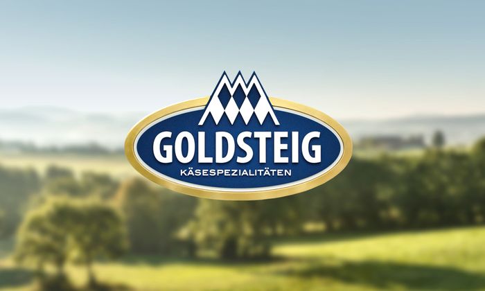 Unternehmenslogo von GOLDSTEIG, im Hintergrund Wald und Wiesen