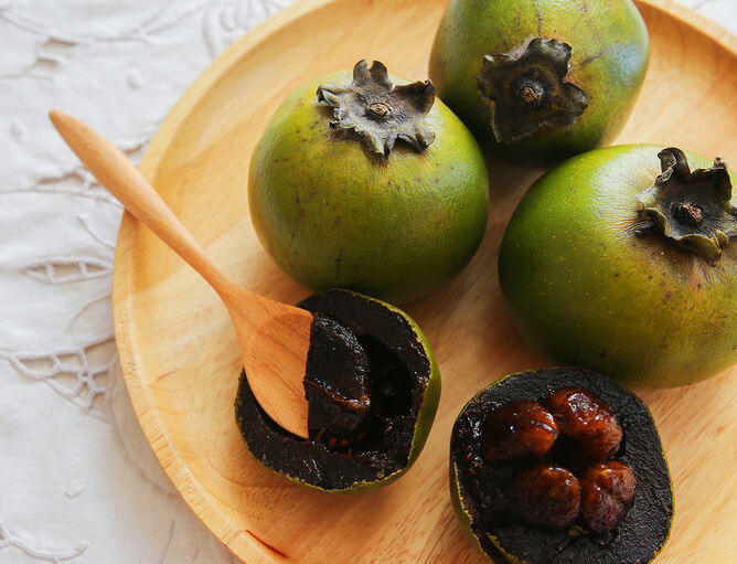 Schwarze Sapote Frucht im Ganzen und aufgeschnitten auf Holzschale 
