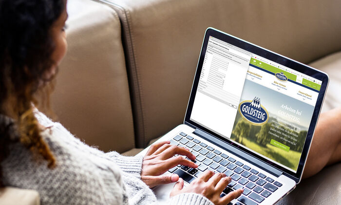 Zu Ihrer Bewerbung/bewerbe: Potenzielle Bewerberin sitz auf ihrer Coach und trägt ihre persönlichen Daten in das Online-Bewerbungsformular der GOLDSTEIG Käsereien ein.