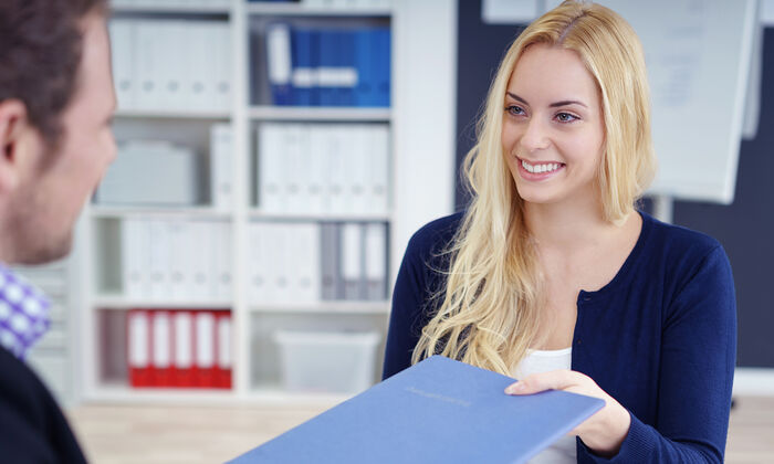 Infos zur Bewerbung: Vorstellungsgespräch einer jungen Frau. Diese überreicht dem Recruiter ihre Bewerbung.