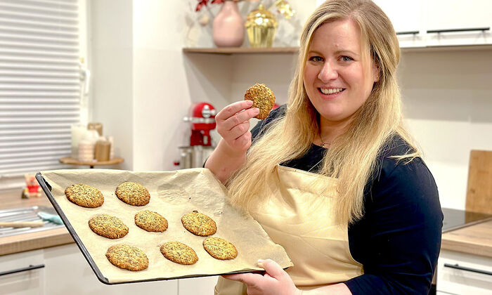 Rezepte & Inspirationen: Monika Nagl zeigt lächelnd ihre gesunden Cookies mit Chiasamen, Leinsamen und Butter auf einem mit Backpapier ausgelegten Backblech.