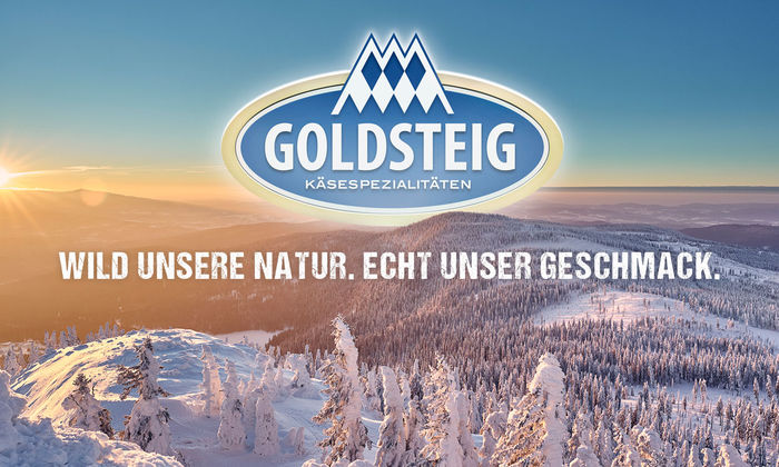 Startseite: Blick vom Arber in die Weite des winterlichen Bayerischen Waldes. Mittig ist das GOLDSTEIG-Logo, darunter der Slogan "Wild unsere Natur. Echt unser Geschmack.“ zu erkennen.