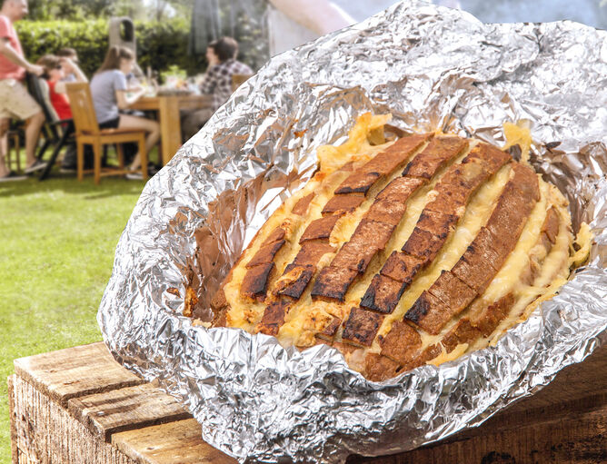 gegrilltes Brot mt Käse von GOLDSTEIG in Alufolie auf Holzkiste im Garten mit Grillgesellschaft