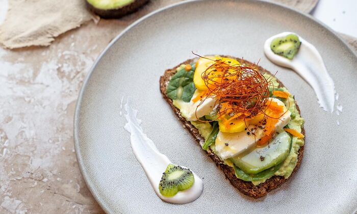 Rezepte & Inspirationen: Avocado-Brot mit Mango-Kiwi-Mozzarella und Butter von GOLDSTEIG auf grauem Teller.