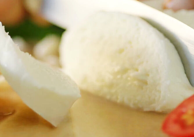 Messer das eine Mozzarella Kugel von GOLDSTEIG auf einem Holzbrett schneidet - ein Pasta Filata Käse