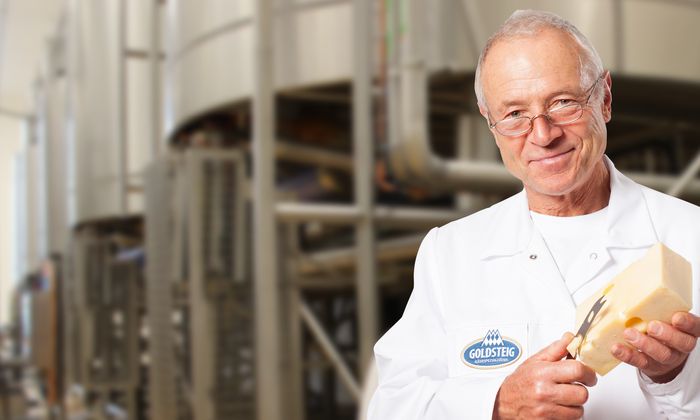 Meister der Käsereifung der Käsemeister von GOLDSTEIG mit Messer und Emmentaler in der Hand in der Produktion