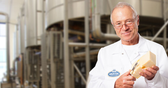 Meister der Käsereifung der Käsemeister von GOLDSTEIG mit Messer und Emmentaler in der Hand in der Produktion