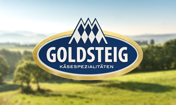 GOLDSTEIG als Arbeitgeber/Schüler/Studenten/Berufseinsteiger/Berufserfahrene/Stellenangebote/Infos zur Bewerbung/FAQ: Bayerische Landschaft mit Wiesen und Wälder. Im Vordergrund sieht man das GOLDSTEIG Logo.