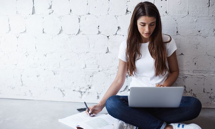 Bachelorarbeit / Masterarbeit: Studentin sitzt am Boden und recherchiert für ihre Arbeit am Laptop 