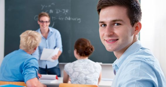 Karriere: Ein Schüler blickt sitzend im Klassenzimmer über seine Schulter in die Kamera. Im Hintergrund sieht man seine Schulkameraden.