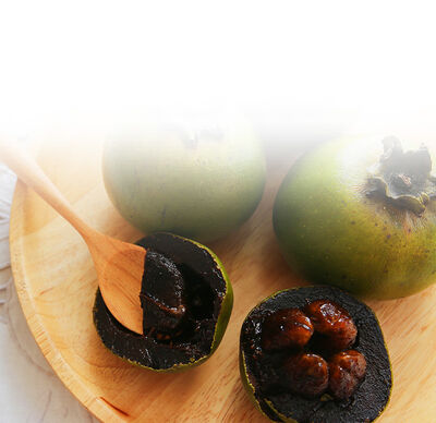 Schwarze Sapote Frucht im Ganzen und aufgeschnitten auf Holzschale 