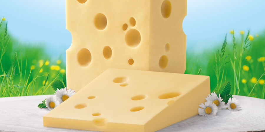 Tipp: Schneiden Sie die Rinde ab - GOLDSTEIG Käsespezialitäten Emmentaler Stück von GOLDSTEIG ohne Rinde mit Gänseblümchen vor Blumenwiese