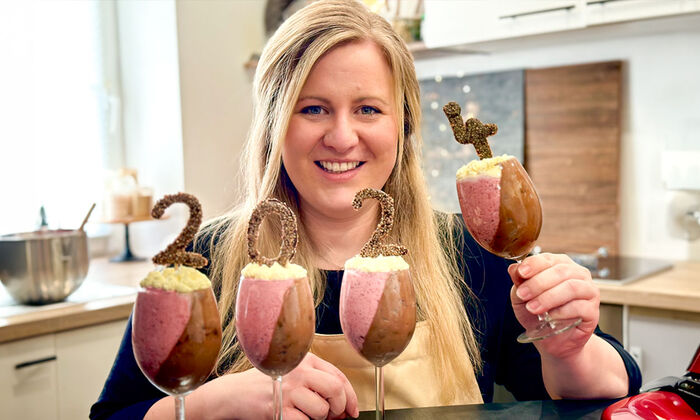 Rezepte & Inspirationen: Monika Nagl zeigt lächelnd ihr Silvester-Dessert Zweierlei Mousse mit Mascarpone. In den Dessertgläsern stecken die Jahreszahlen.