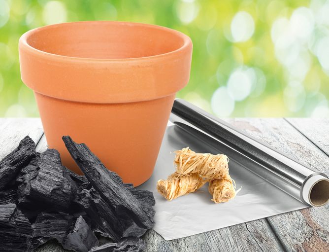 Aktionen und Neues: Grill aus Blumentopf - GOLDSTEIG Käsespezialitäten Grill aus Blumentopf, Alufolie, Holzanzünder und Gillkohle auf Holztisch um GOLDSTEIG Produkte zu grillen